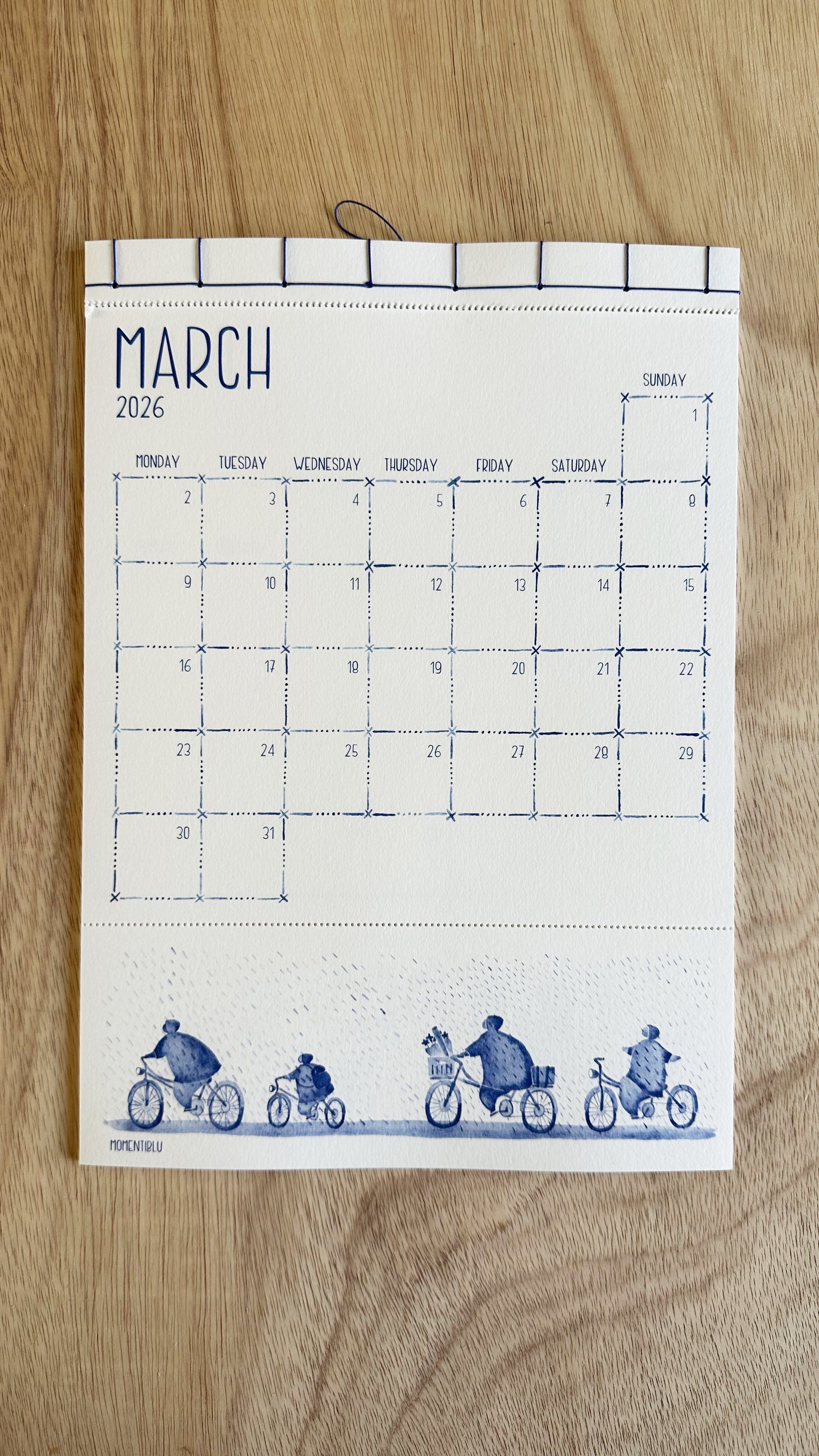 March calendar with blue illustrations of people on bicycles on a wooden surface